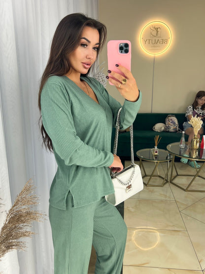 Woman in a green outfit taking a mirror selfie in a stylish room.
