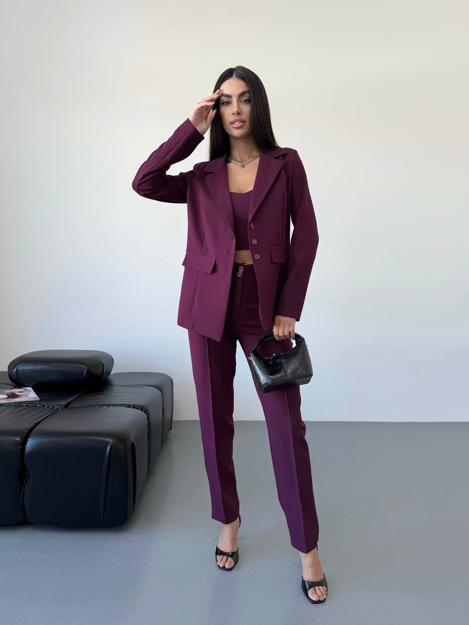 Woman in a purple suit standing in a minimalistic room with a black sofa.