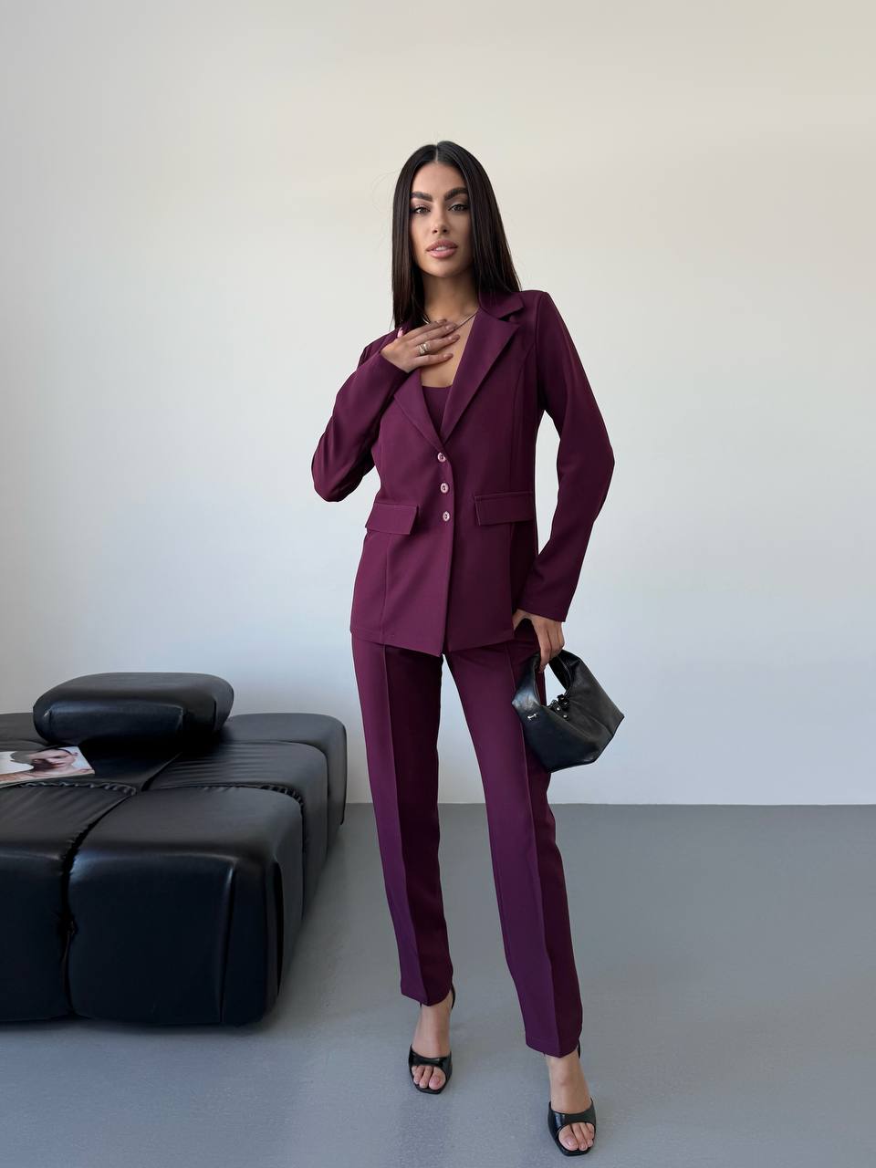 Woman in a purple suit standing in a minimalistic room with a black sofa.