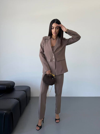 Woman in a brown suit standing in a minimalistic room with a black sofa.