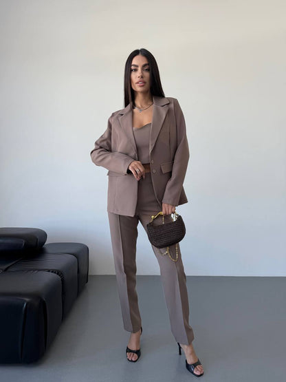 Woman in a brown suit standing in a minimalistic room with a black sofa.