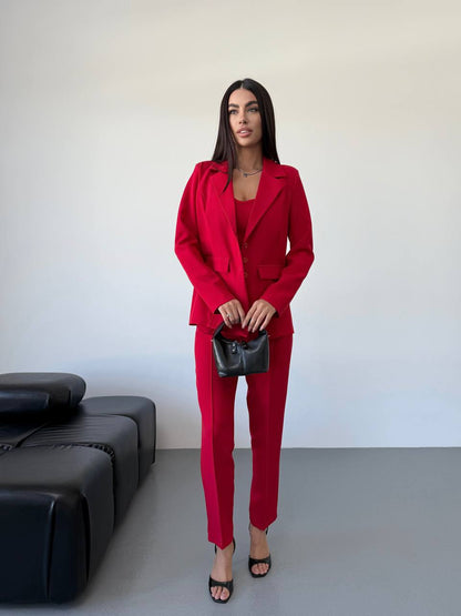 Woman in a red suit standing in a minimalistic room with a black couch.