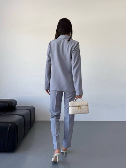 Person wearing a gray suit holding a beige handbag in an indoor setting.