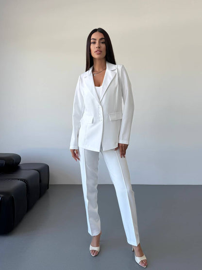 Woman wearing a white suit standing in a minimalistic room with a black sofa.