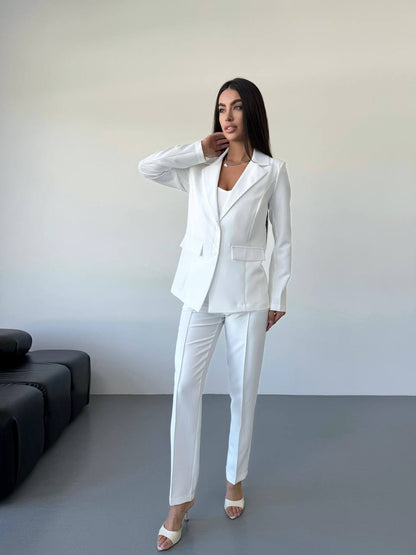 Woman wearing a white suit standing in a minimalistic room with a gray floor and black sofa.