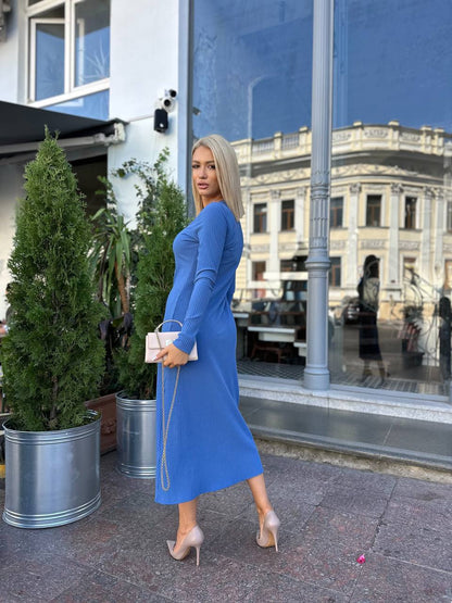 Woman in a blue dress standing outdoors with a building and plants in the background