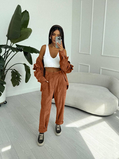 Woman taking a mirror selfie wearing a white top and brown pants in a modern room.