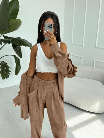 Person wearing a white top and brown pants with a beige cardigan in a room with a plant and sofa.