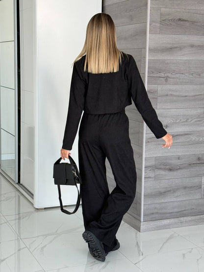 Person wearing a black outfit with a matching handbag in a modern interior setting.