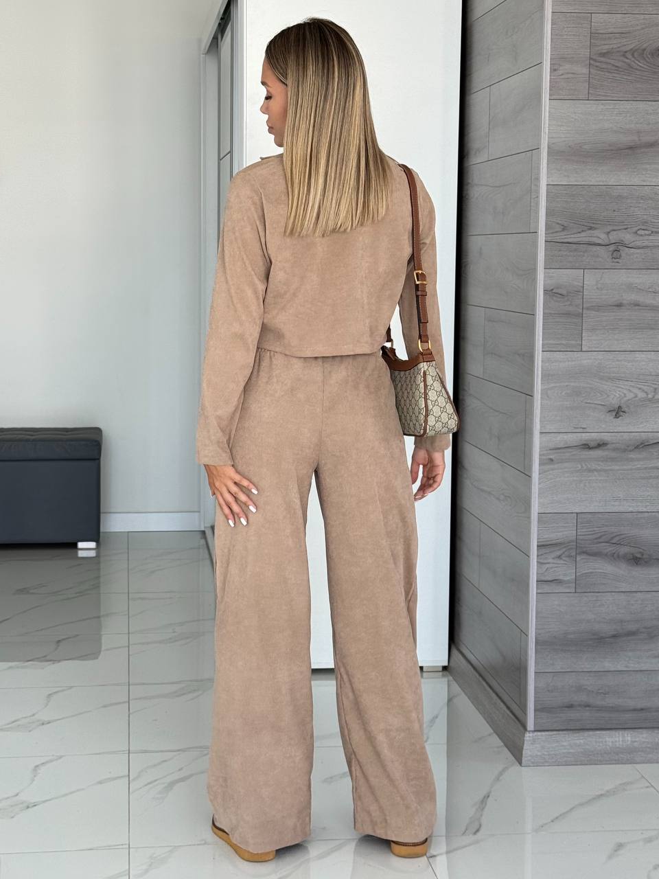 Woman in a beige outfit standing in a modern interior setting.