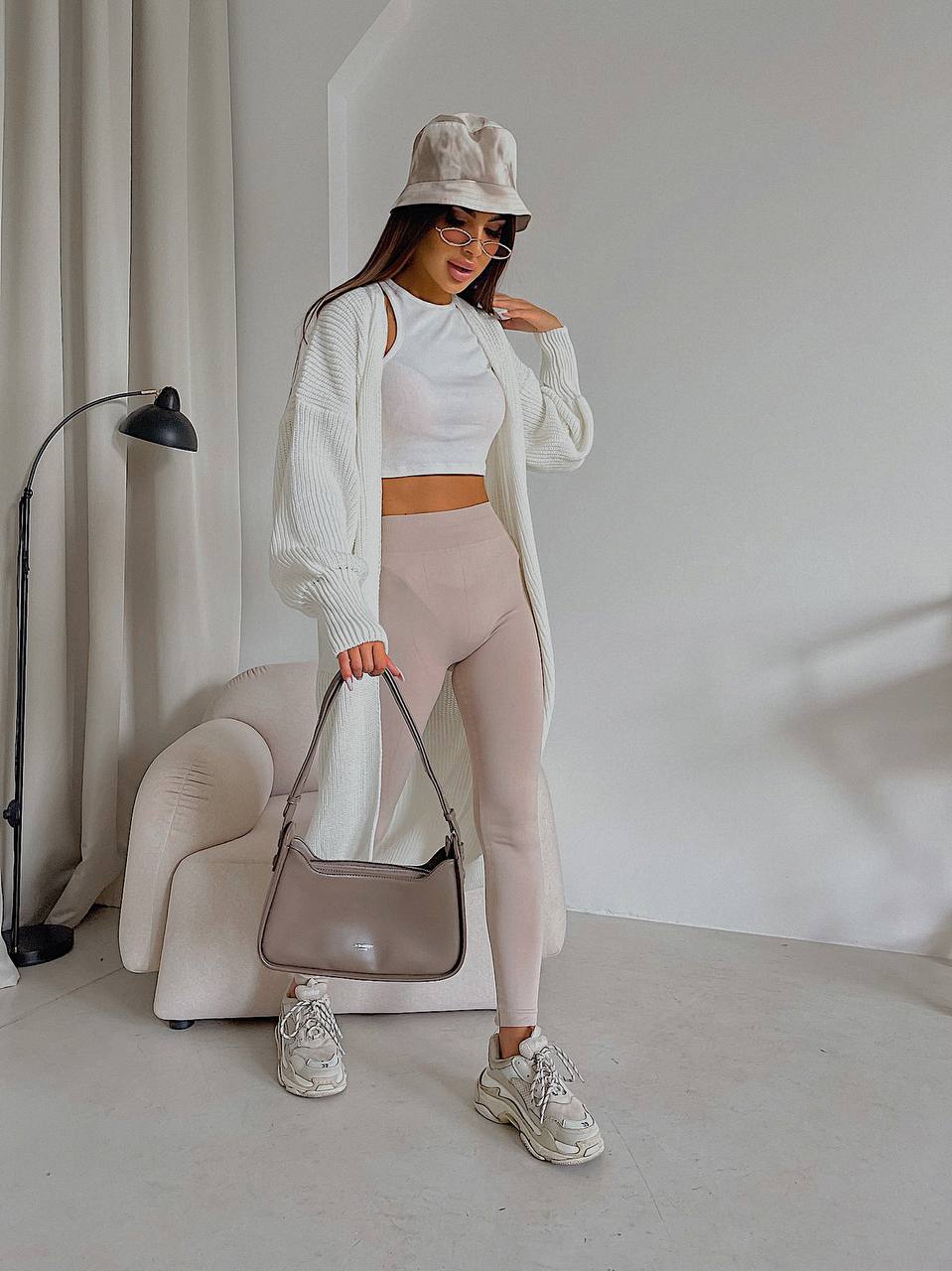 Woman in a white outfit with beige accessories in a minimalistic room.