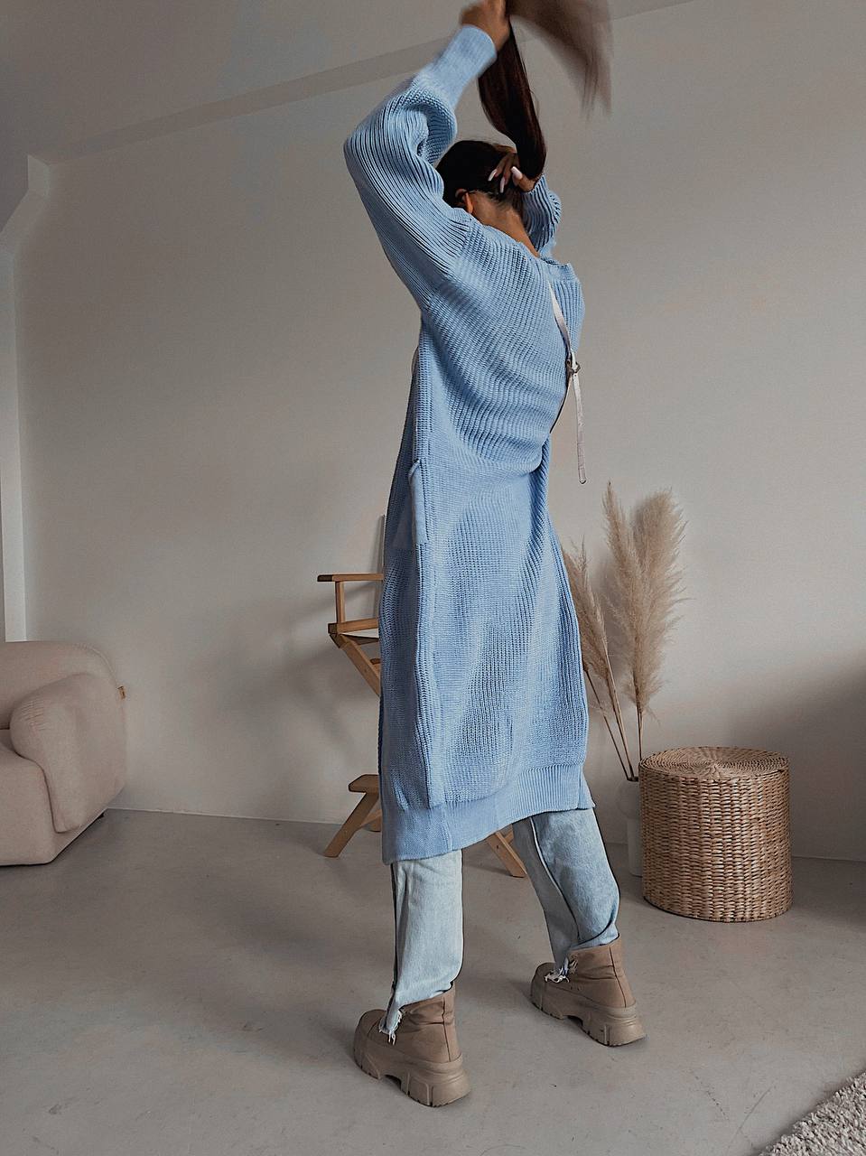 Person wearing a long light blue cardigan in a minimalistic room.