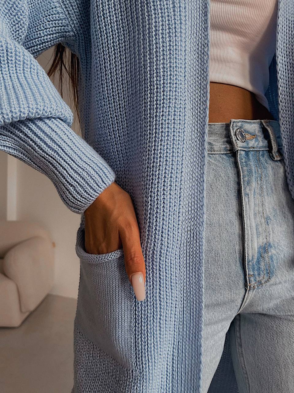 Person wearing a blue knitted cardigan and jeans with a blurred background