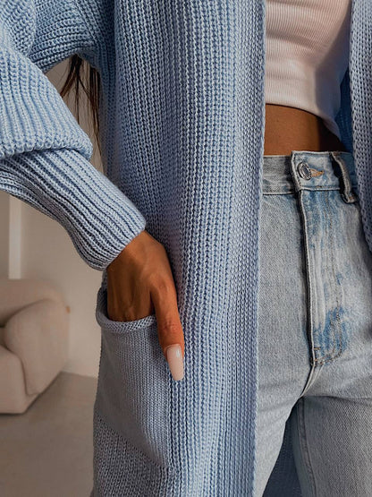 Person wearing a blue knitted cardigan and jeans with a blurred background