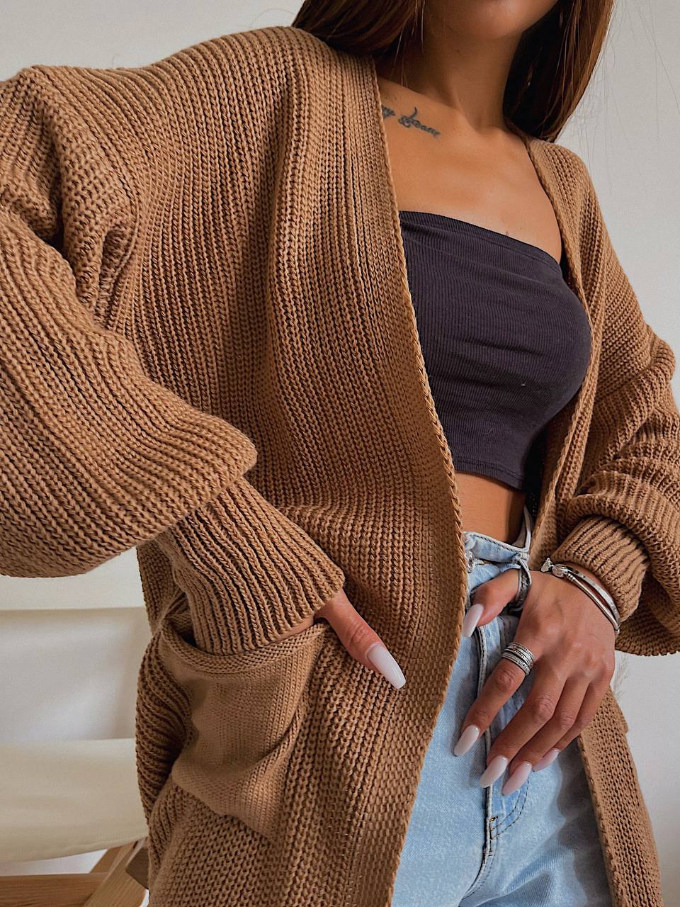 Person wearing a brown knitted cardigan over a dark top and light blue jeans.