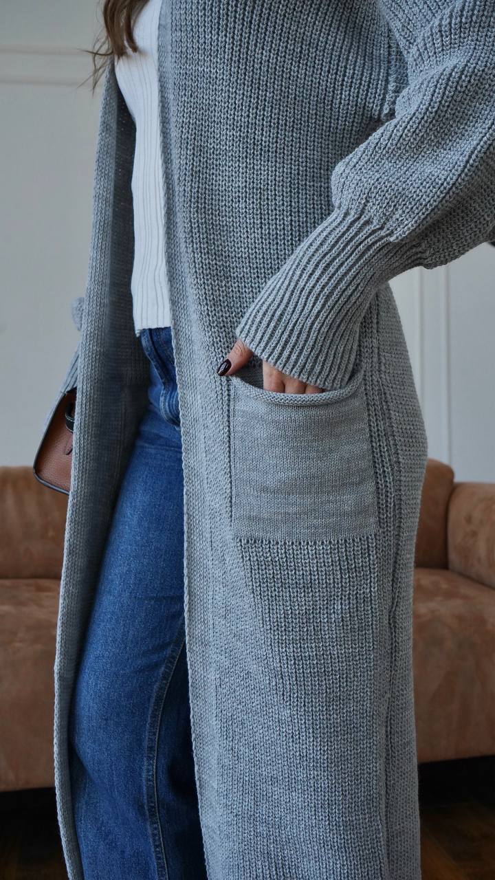 Person wearing a long gray cardigan and blue jeans indoors.