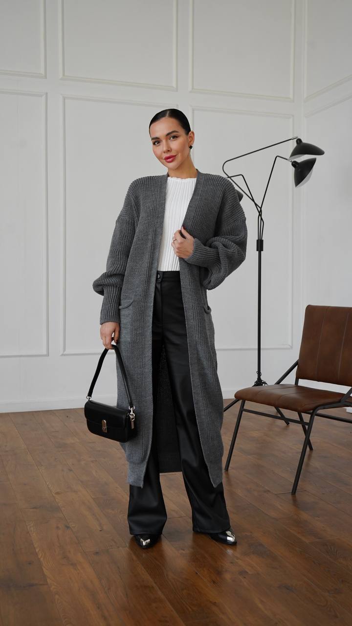 Woman wearing a long gray cardigan in a room with wooden floor and white walls.