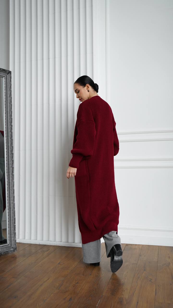 Person wearing a long burgundy sweater in a minimalistic room.