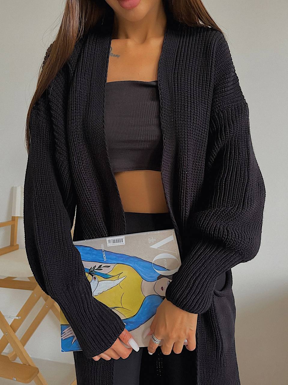 Person wearing a black cardigan over a dark top, holding a colorful book.