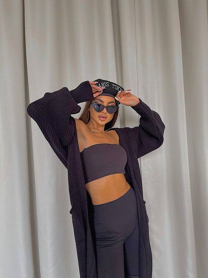 Person wearing a dark purple outfit with a matching cardigan against a neutral background