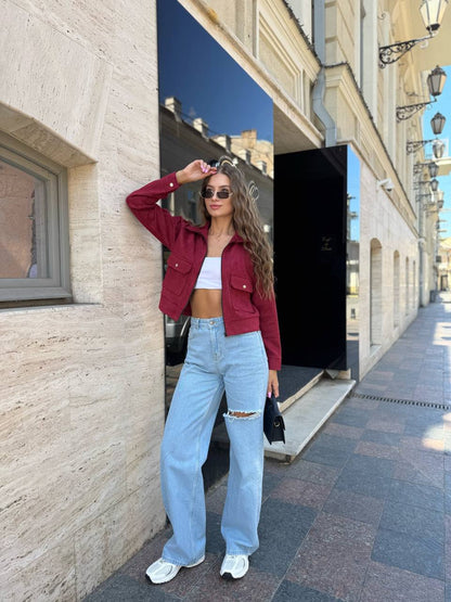 Woman in a red jacket and light blue jeans standing on a street with buildings in the background