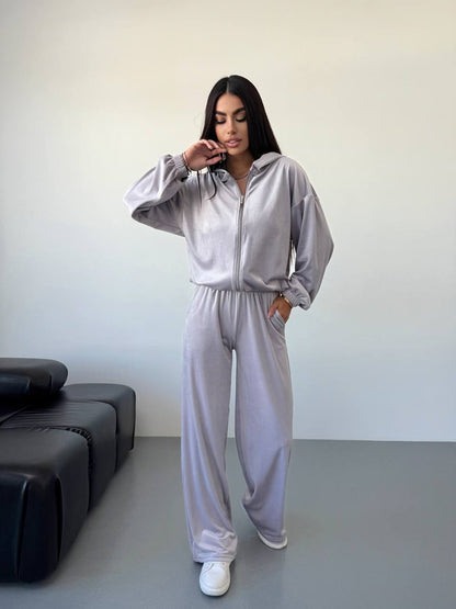 Person wearing a light gray tracksuit in a minimalistic room.