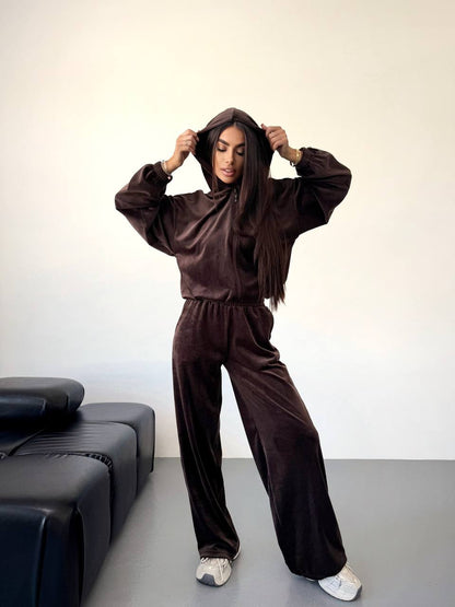 Person wearing a brown tracksuit standing in a minimalistic room with a black sofa.