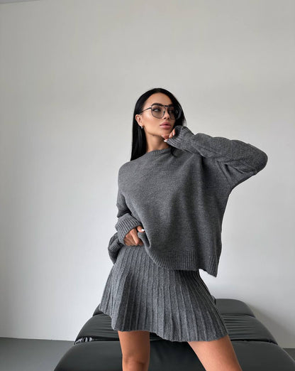 Woman wearing a gray sweater and skirt against a plain background