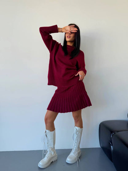 Person wearing a maroon sweater and skirt with white boots against a plain background