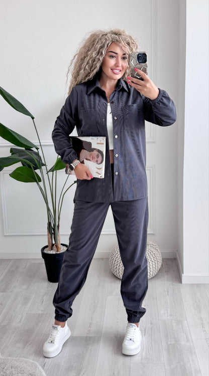 Woman taking a mirror selfie wearing a dark gray outfit with white sneakers in a room with a plant and decorative items.