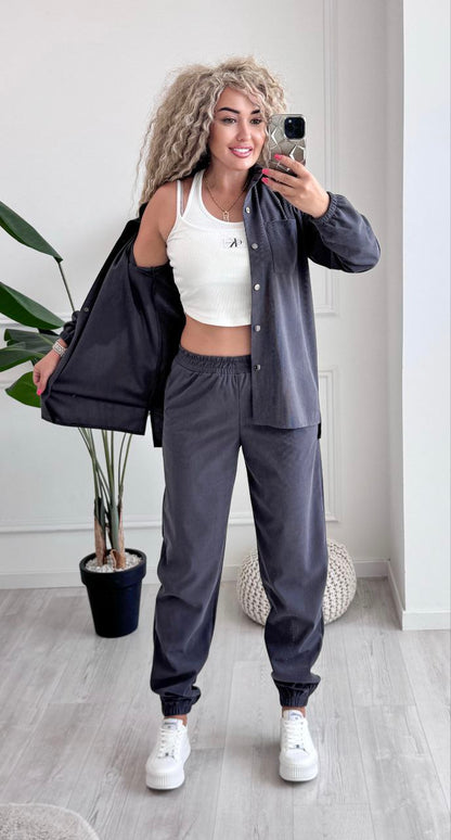 Woman taking a mirror selfie wearing a gray tracksuit and white sneakers in a minimalistic room.