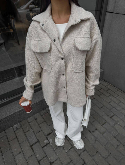 Person wearing a beige sherpa coat with a white shirt and pants, holding a red cup and a white bag.
