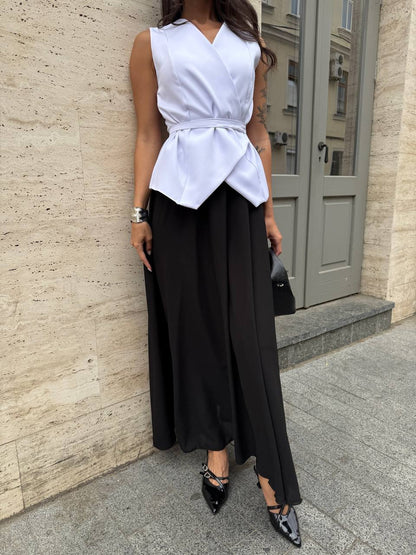 Woman wearing a white sleeveless top and black wide-leg pants against a beige wall.