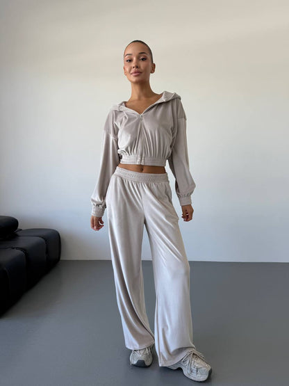 Person wearing a light gray outfit with a cropped top and wide-leg pants in a minimal room.