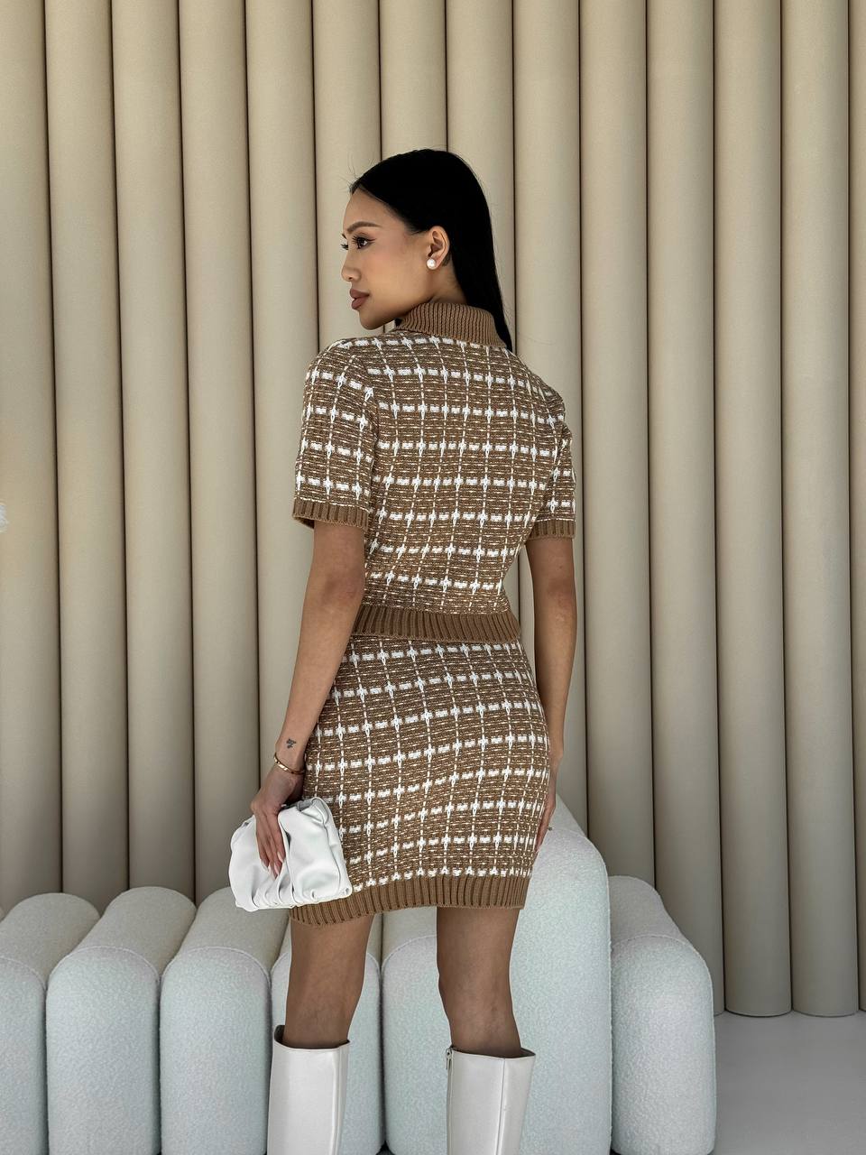 Woman wearing a patterned dress and white boots against a neutral background
