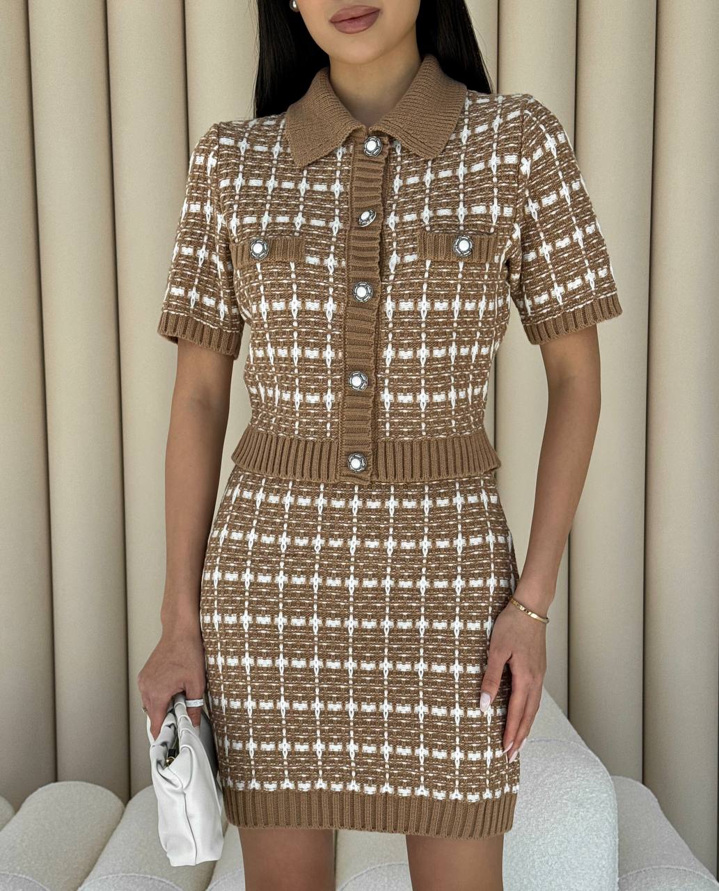 Woman wearing a brown and white checkered dress with a collar, holding a white clutch.