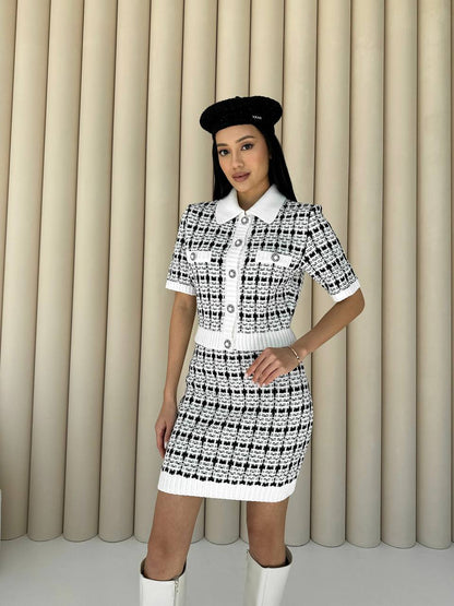 Woman wearing a black and white patterned dress with a beret against a beige curtain background