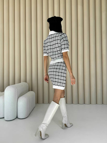Person wearing a black and white patterned outfit with knee-high boots in a minimalistic room.