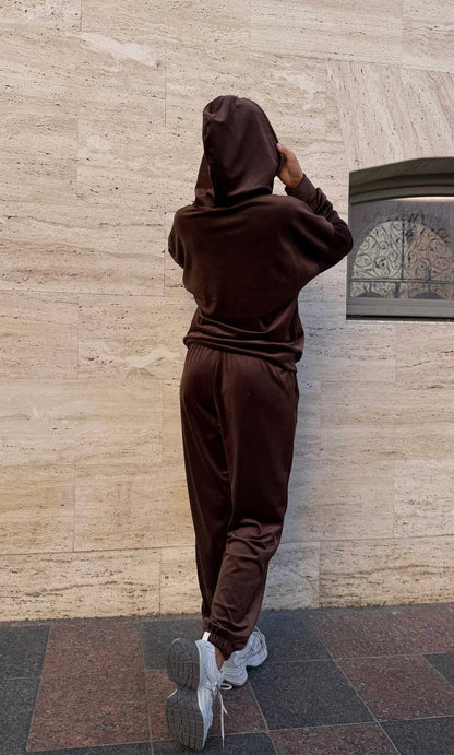 Person wearing a brown tracksuit standing against a beige wall.
