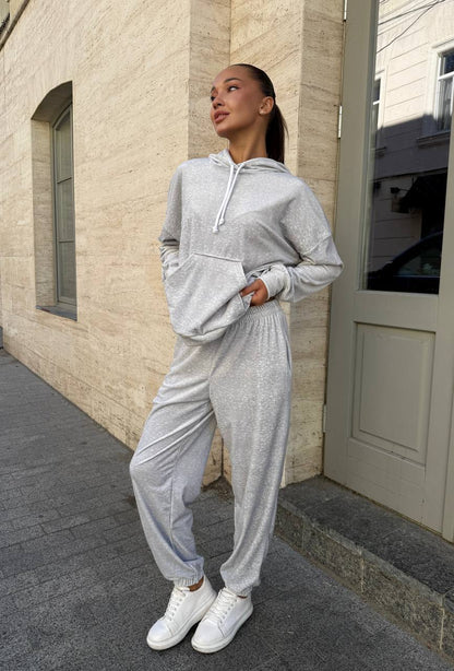 Woman in a gray tracksuit standing on a sidewalk next to a building.