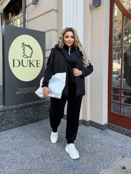 Woman in black outfit holding a white bag in front of a building with 'DUKE' signage.