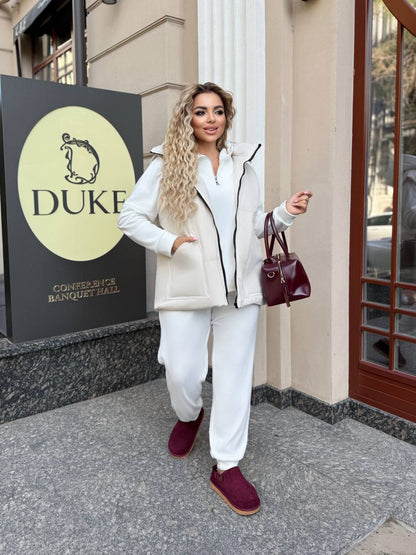 Woman in white outfit with burgundy shoes standing in front of a building with 'DUKE' sign.
