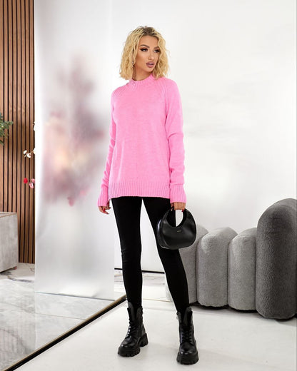 Woman wearing a pink sweater and black pants in a modern room.