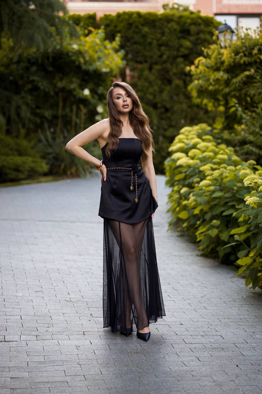 Woman in a black outfit standing on a paved path with greenery around