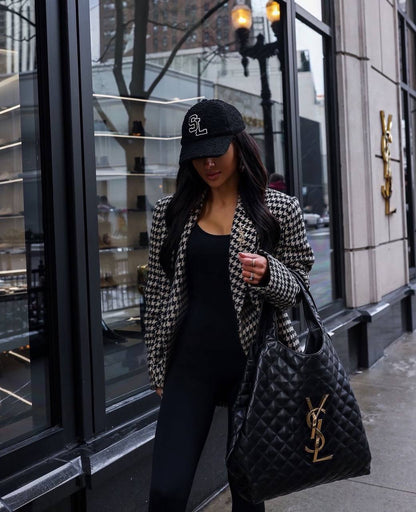 Woman in a houndstooth blazer and black cap holding a YSL bag on a city street.