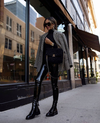 Woman in a checkered blazer and black leather pants standing on a city street.