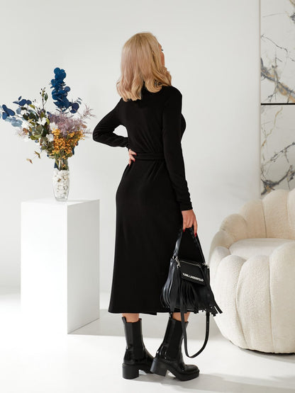 Woman in a black dress holding a black handbag in a minimalistic room.