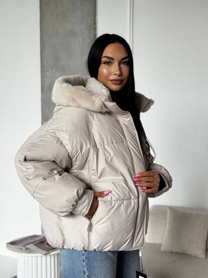 Woman wearing a beige puffer jacket with fur hood in an indoor setting