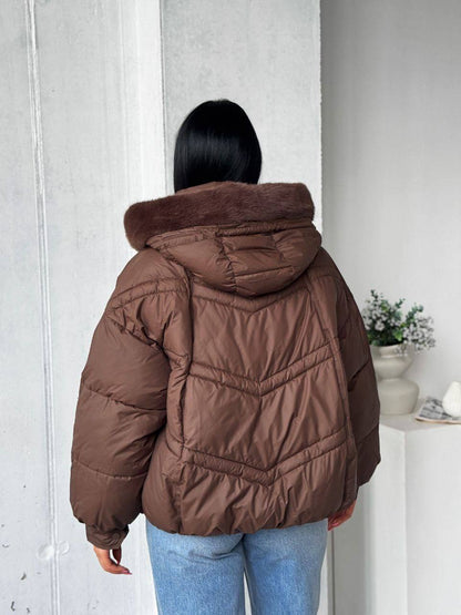 Person wearing a brown puffer jacket with fur hood indoors.