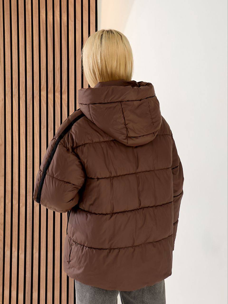 Person wearing a brown puffer jacket standing against a neutral wall.